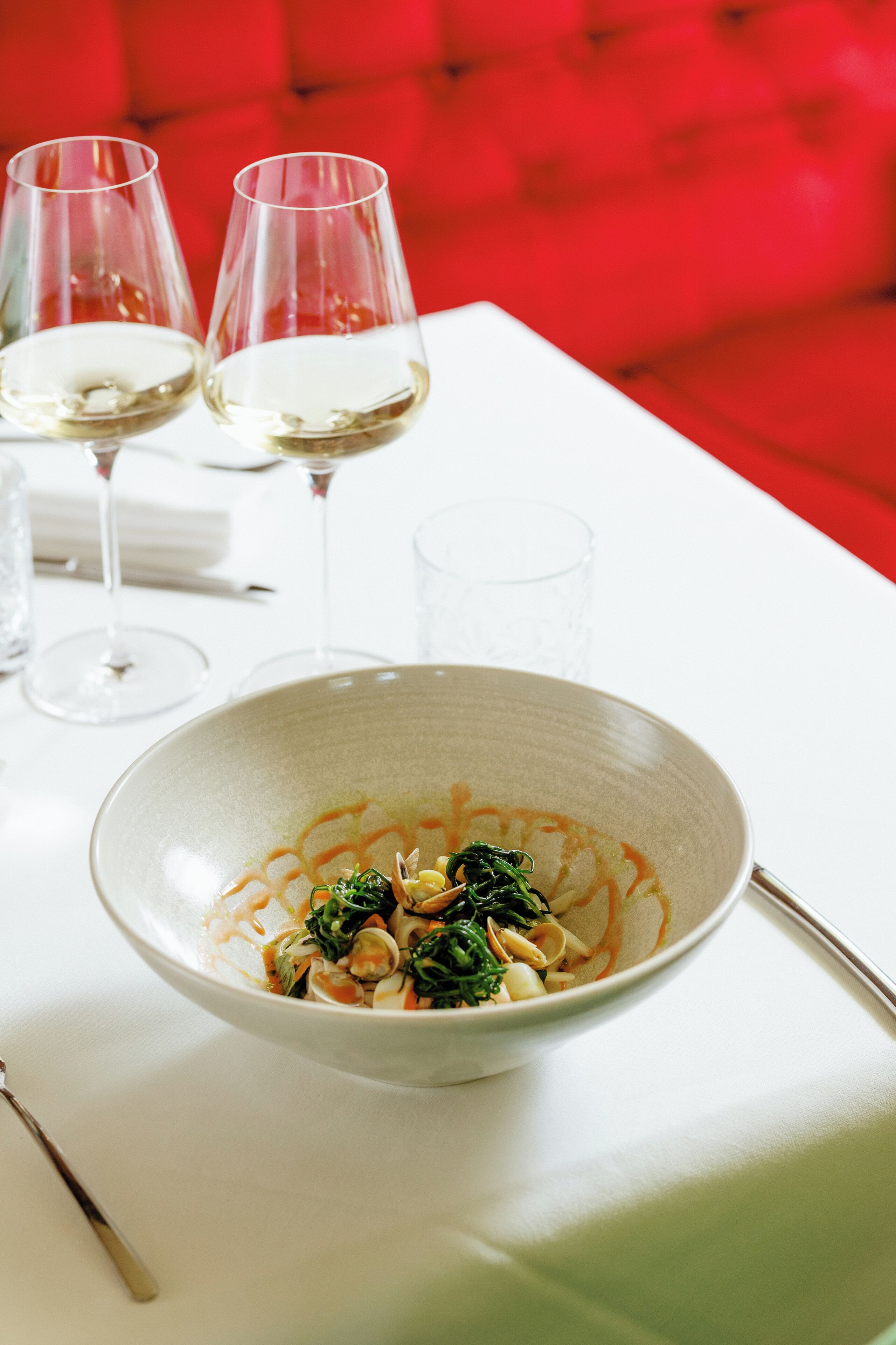 A dining table with a bowl of pasta, two wine glasses, and a spoon.