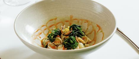 A dining table with a bowl of pasta, two wine glasses, and a spoon.