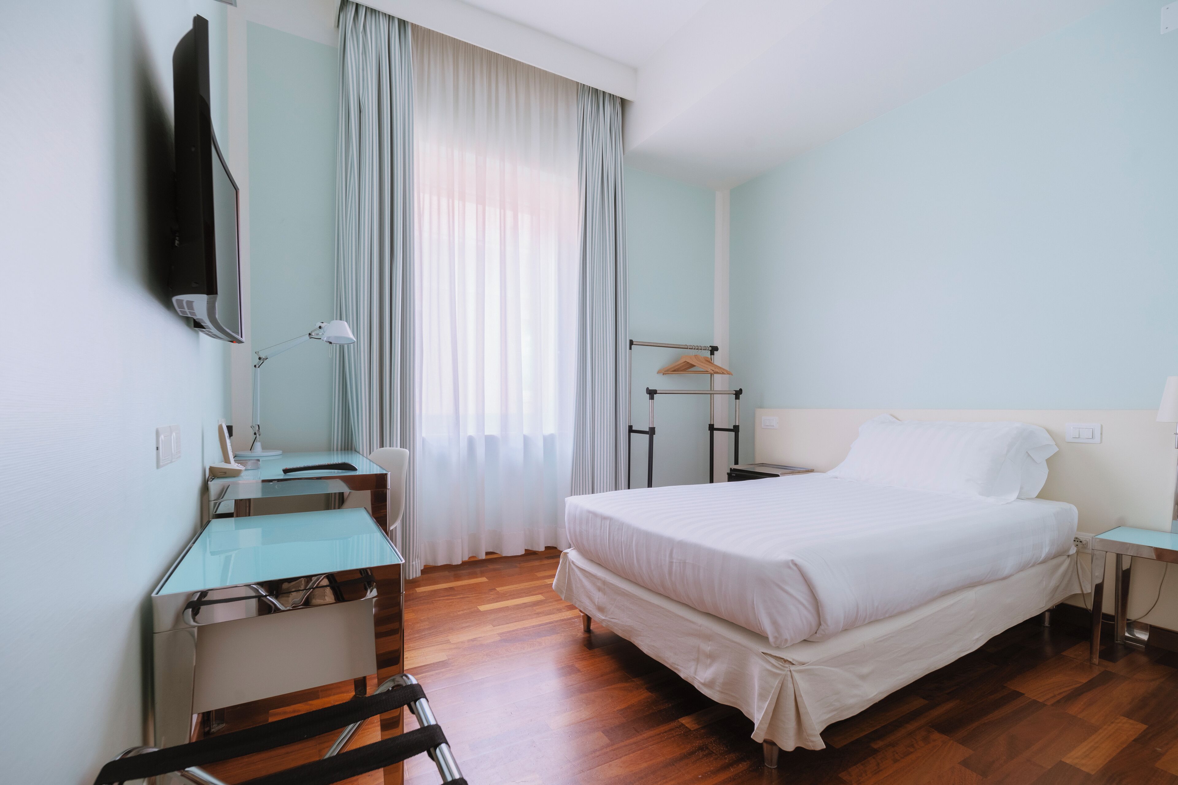 A hotel room with a bed, a desk, a chair, a TV, and a window with curtains.