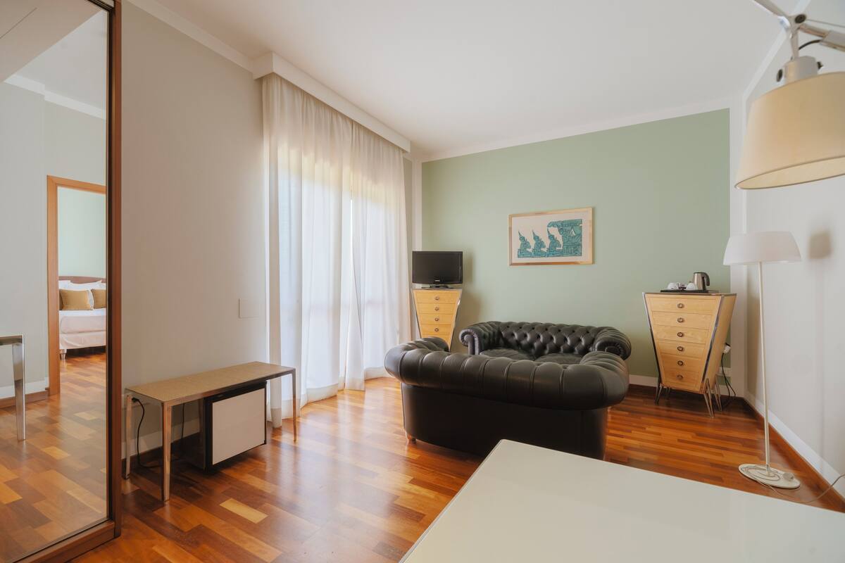 A modern living room with a black leather sofa, a wooden cabinet, a small table, and a TV on a stand.