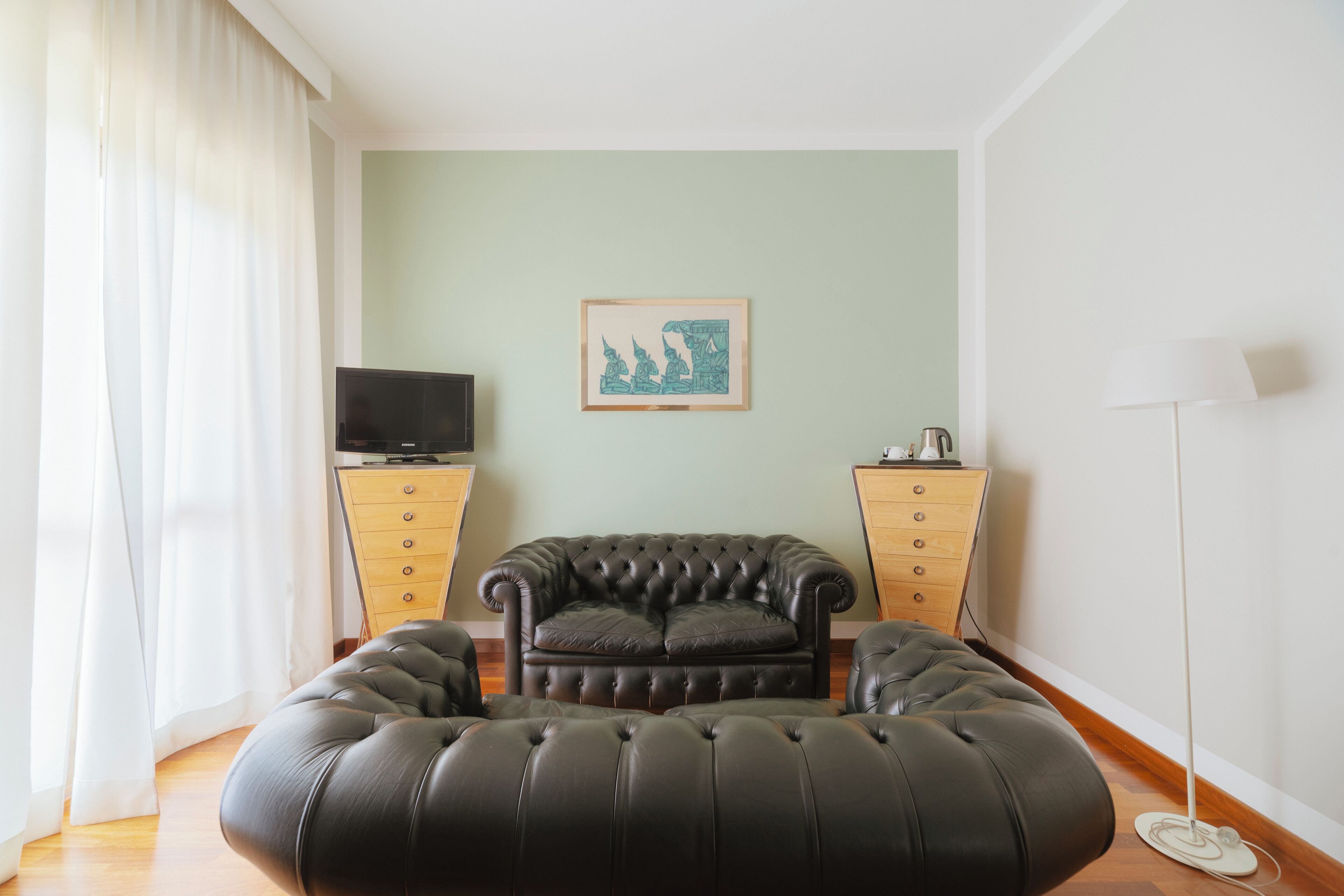 A living room with a black leather sofa, a flat-screen TV on a wooden cabinet, and a floor lamp.