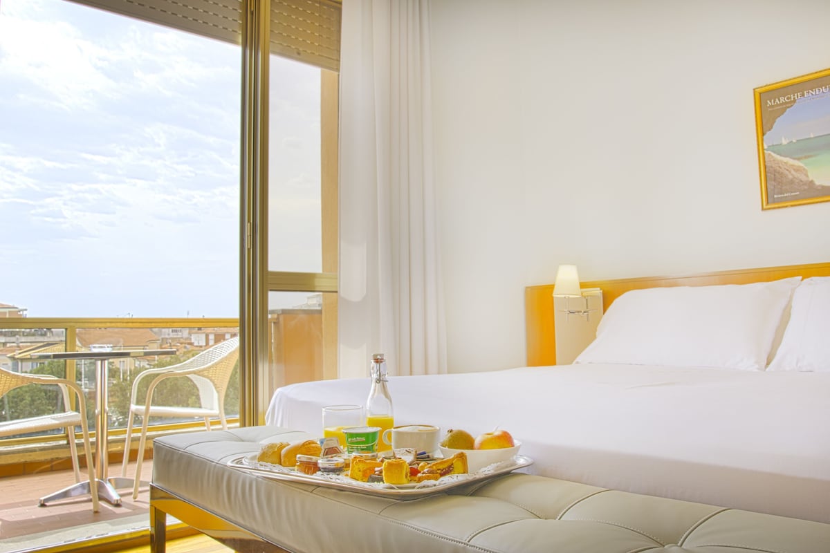 A hotel room with a bed, breakfast tray, and a balcony with chairs.