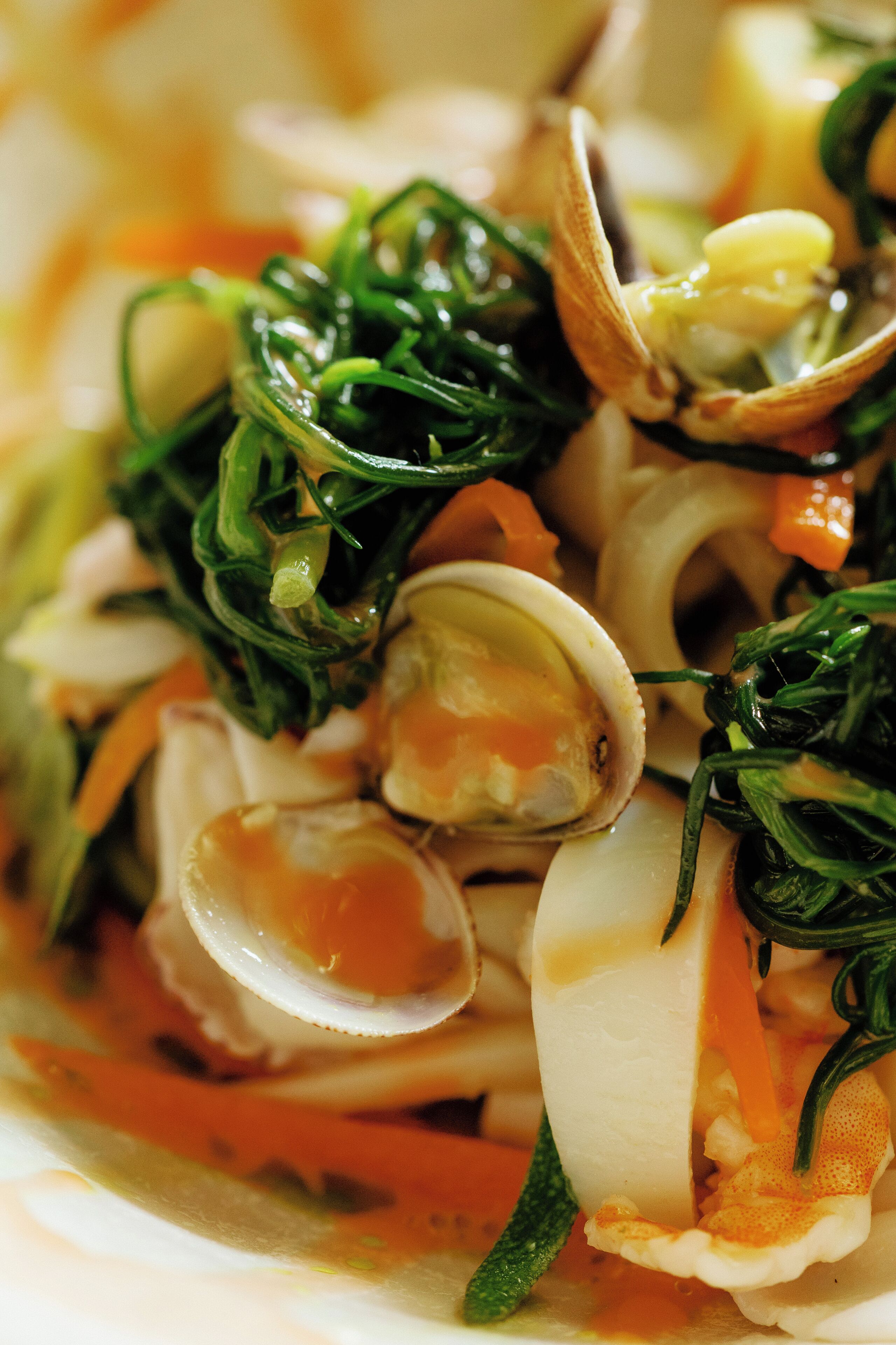 Un primo piano di un piatto con vongole, verdure e salsa.