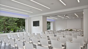 Een congreszaal met rijen witte stoelen, een groot scherm en een beamer.