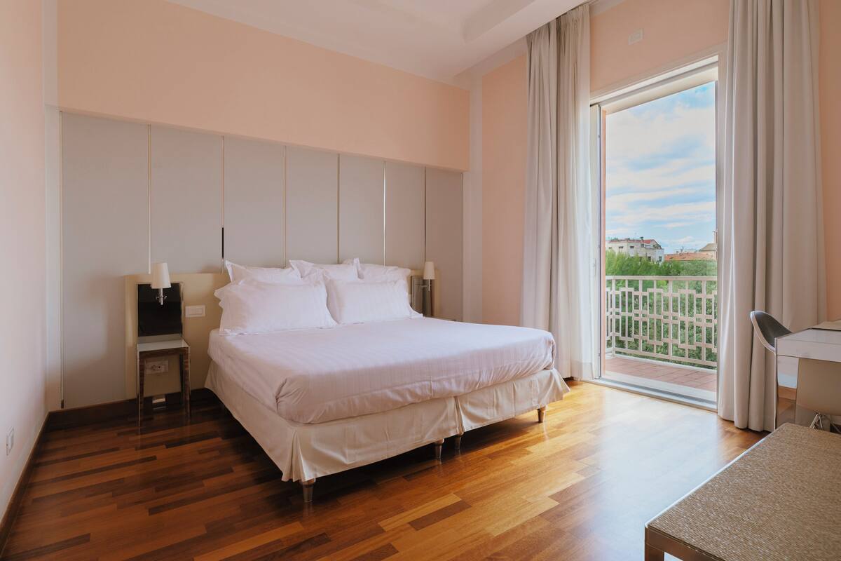 A bedroom with a large bed, a desk, and a view of a balcony.
