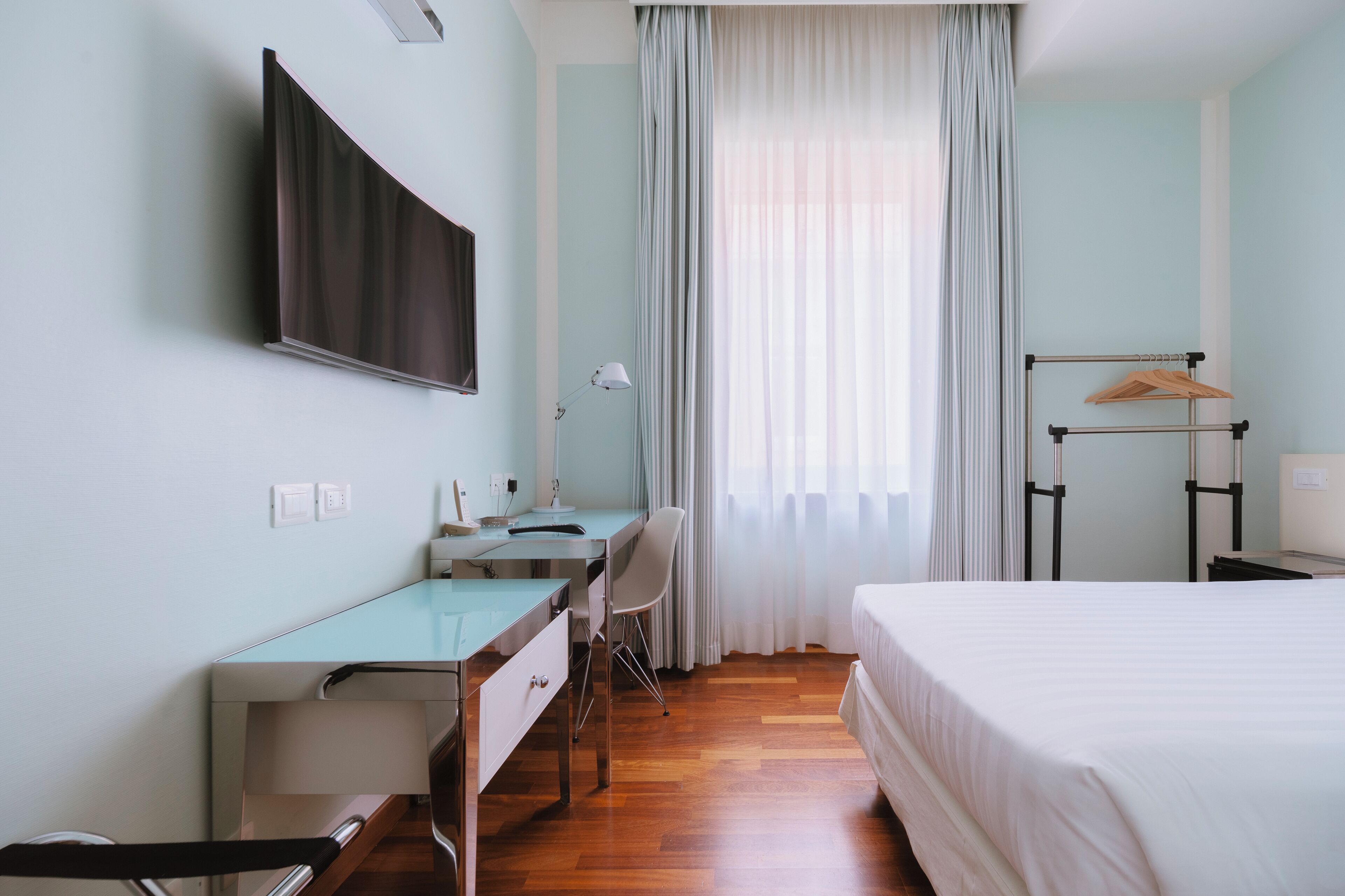 Une chambre d’hôtel équipée d’un lit, d’un bureau, d’une chaise et d’un téléviseur fixé au mur.