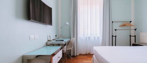 Una habitación de hotel con cama, escritorio, silla y televisión montada en la pared.