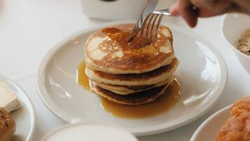 A breakfast setting with pancakes, syrup, a glass of orange juice, and a jar of jam.