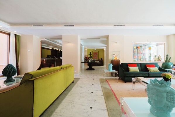 A modern living room with a green sofa, a black sofa with red cushions, and a coffee table. There is a glass display case with decorative items. - Hotel Miramare (Civitanova Marche)