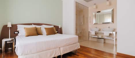 A modern hotel room with a large bed, bedside lamps, a bathroom with a mirror and sink, and wooden flooring.