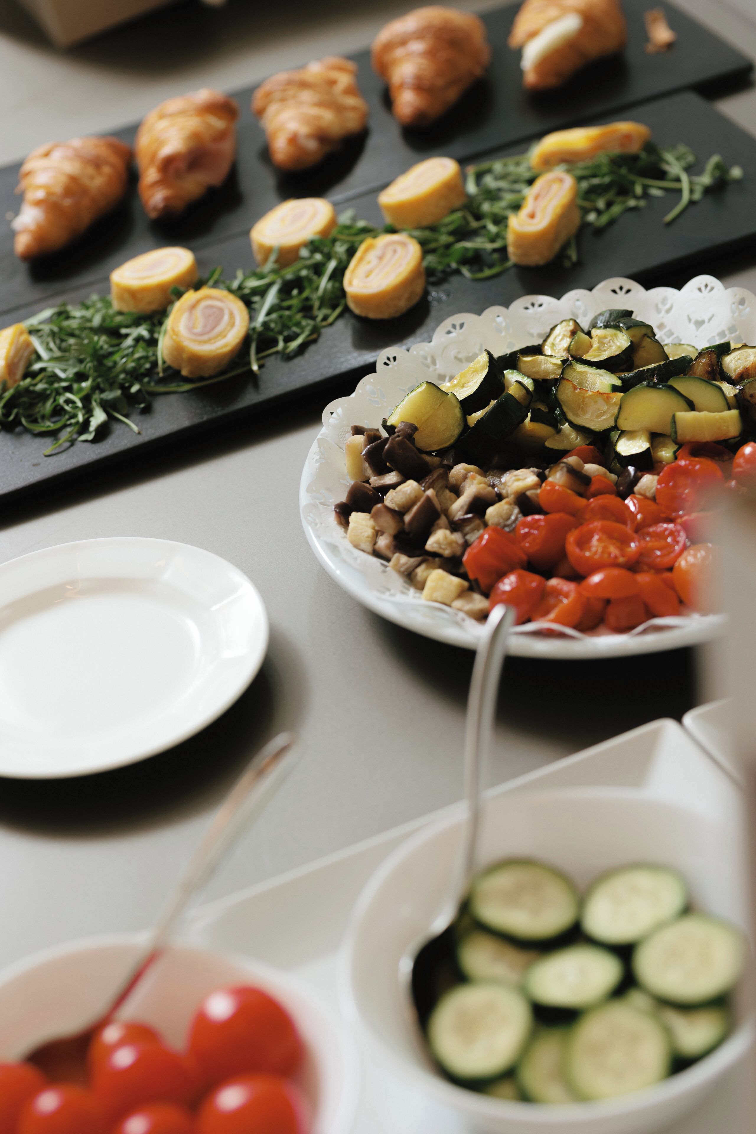 Una mesa de buffet con diferentes alimentos, como cruasanes, verduras y un bol de tomates cherry.