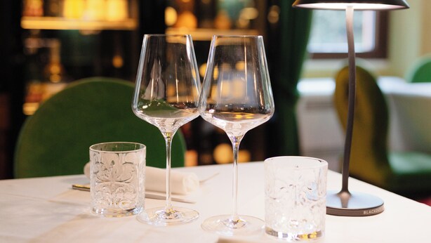 Een gedekte tafel voor diner, met wijnglazen, een waterglas, een lamp en een menukaart.