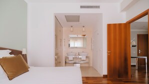 Een hotelkamer met een bed, een houten deur, een badkamer met een spiegel en een wastafel.
