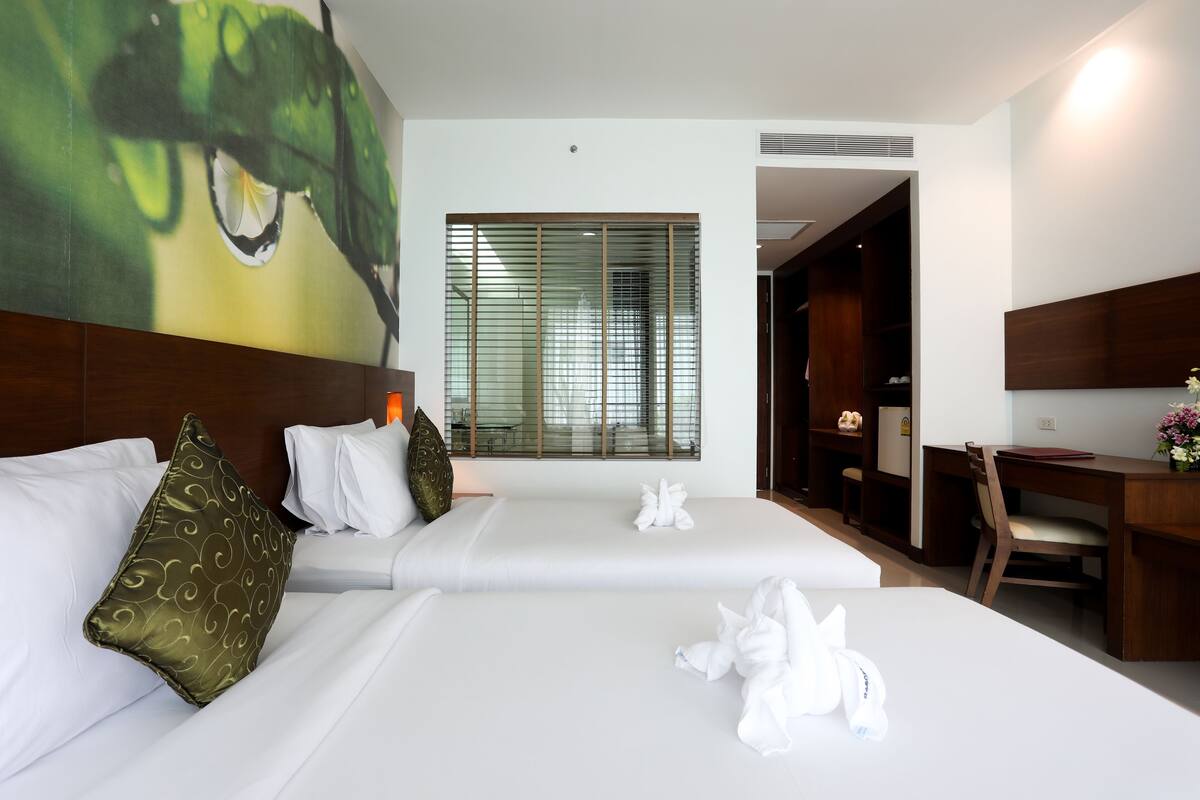 A hotel room with two beds, a large window with blinds, a desk, and a wardrobe.