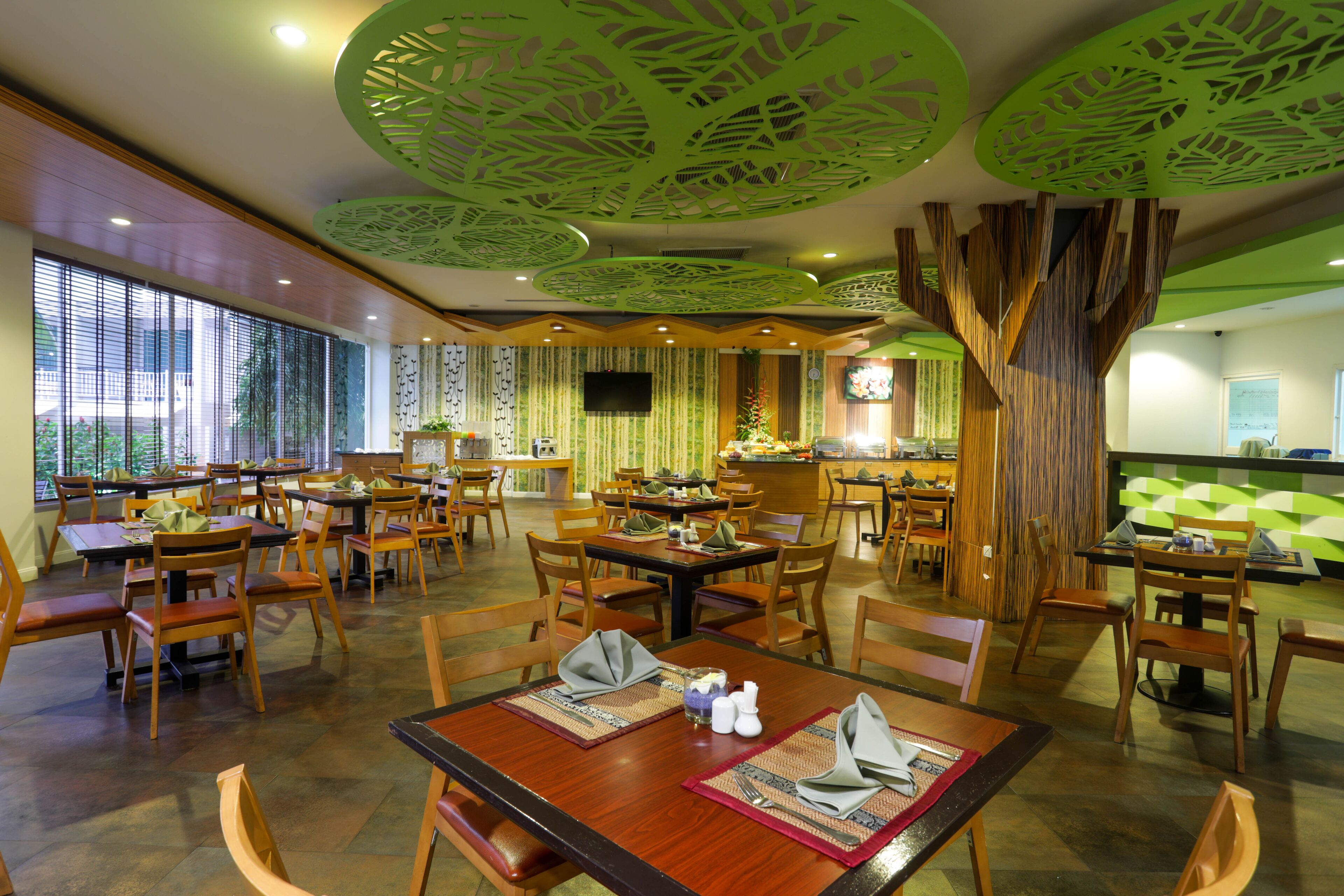 A restaurant with wooden tables and chairs, a green ceiling design, and large windows.
