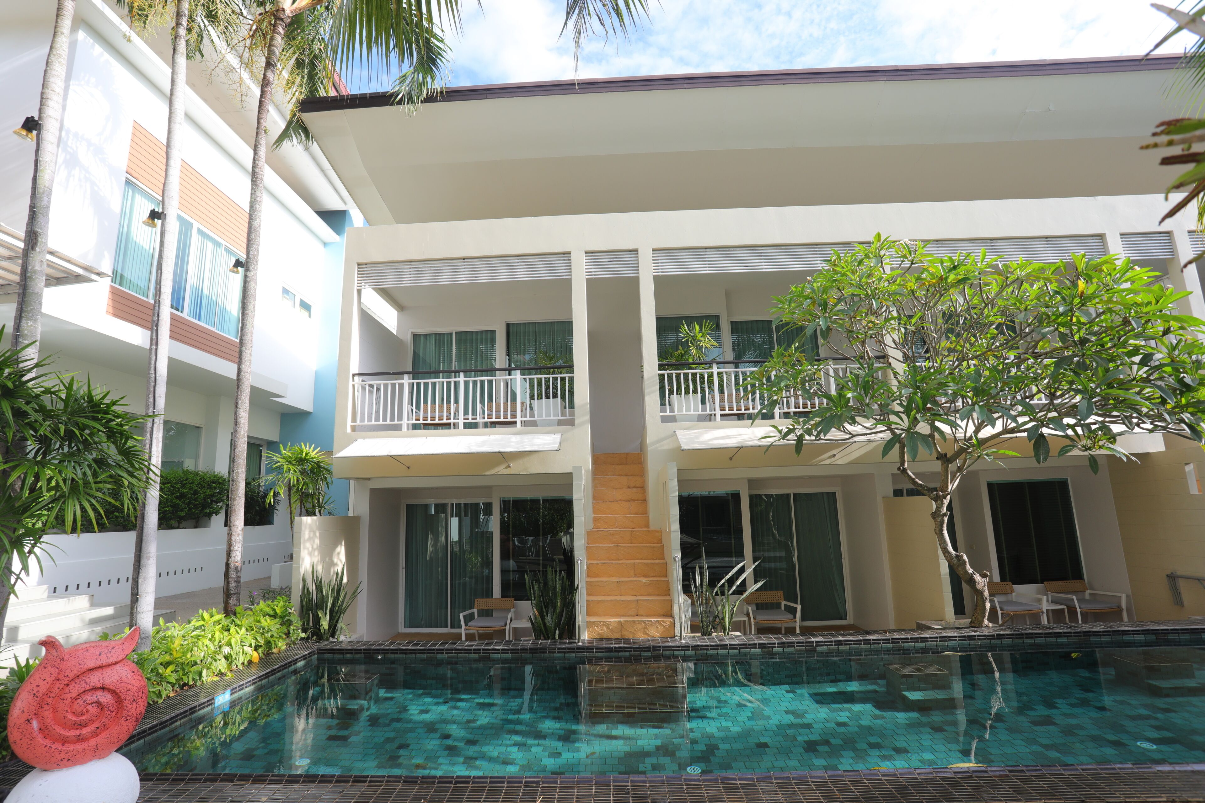 Un hôtel moderne doté d’une piscine, d’un espace extérieur aménagé et d’un escalier menant aux étages supérieurs.