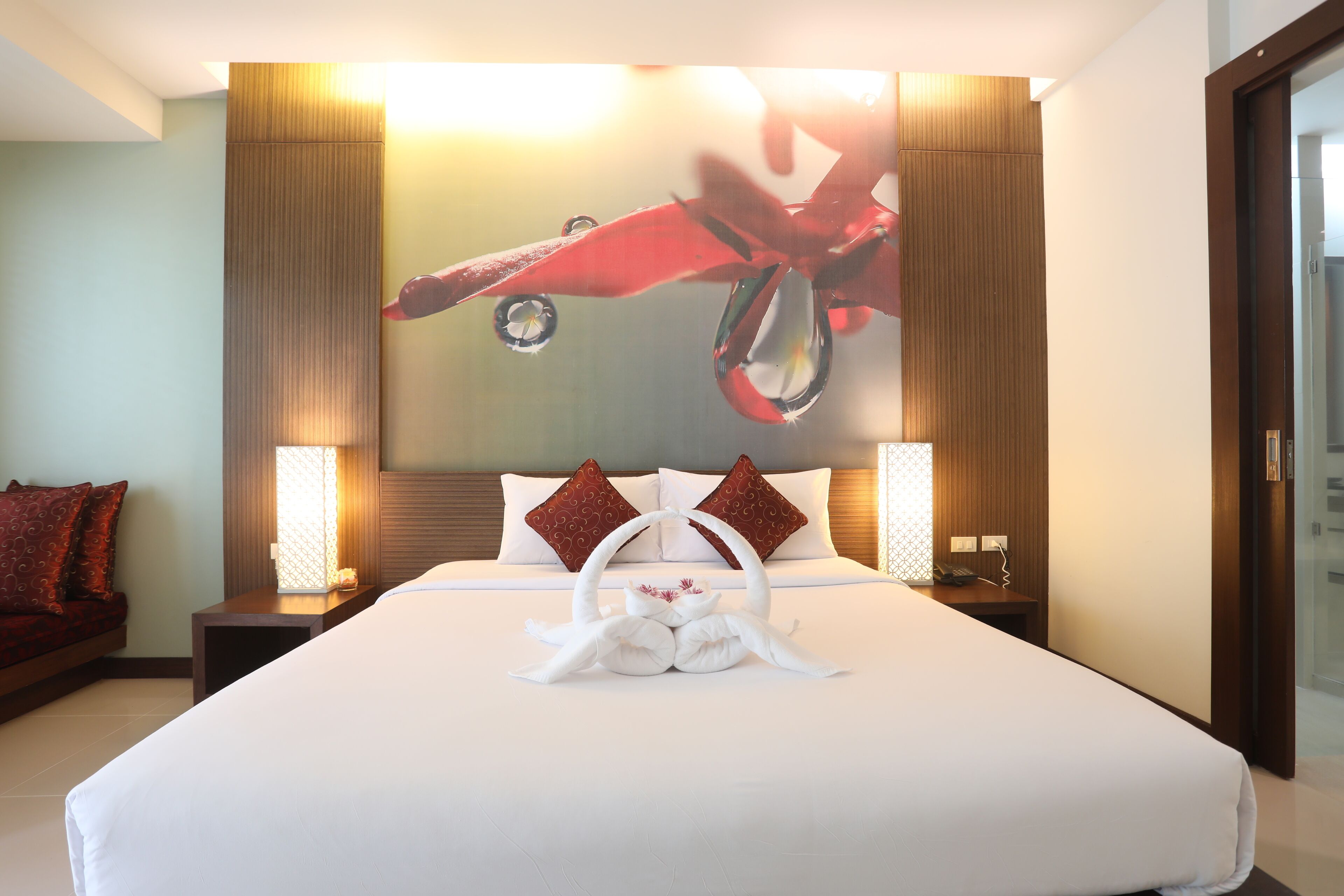 Una habitación de hotel con una cama grande, un cabecero con diseño rojo y blanco, dos mesitas de noche con lámparas y una obra de arte colgada en la pared.