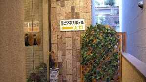 Entrada de un hotel con un muro de piedra, un letrero que indica el camino al vestíbulo, y una celosía de madera decorativa con plantas.