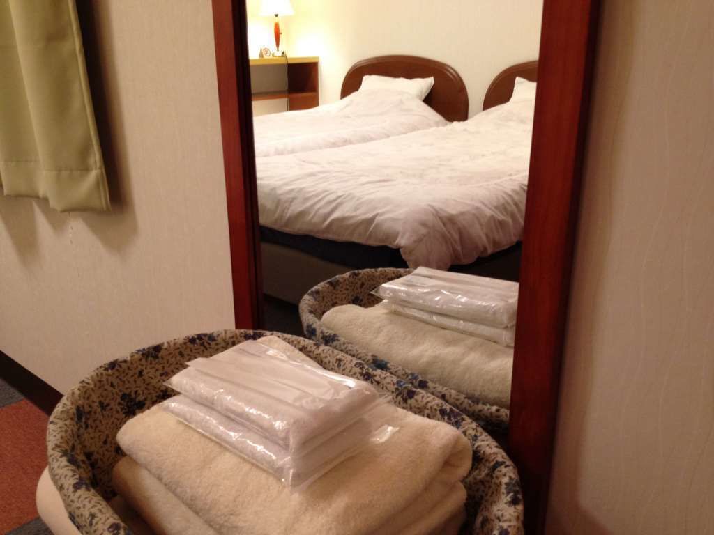 A hotel room with two beds, a mirror reflecting the room, and a bathroom with a towel rack.