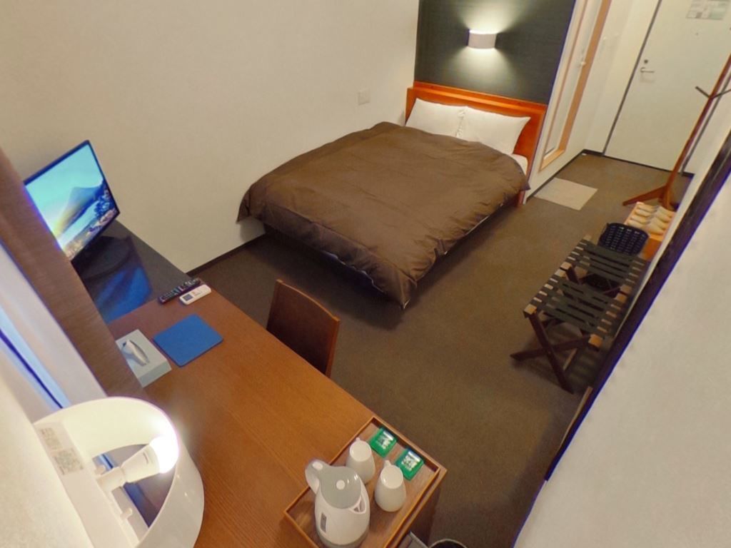 Habitación de hotel con cama, escritorio con computadora, bandeja con tazas de té y una silla.