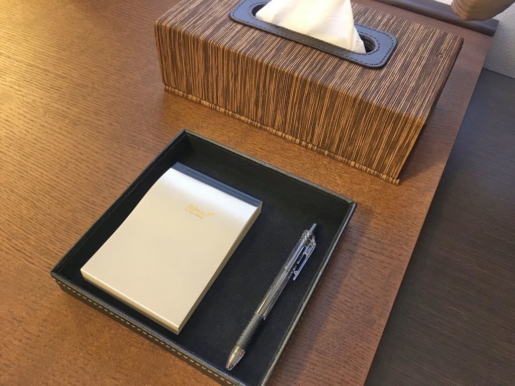 A wooden table with a tissue box, a notepad, and a pen.