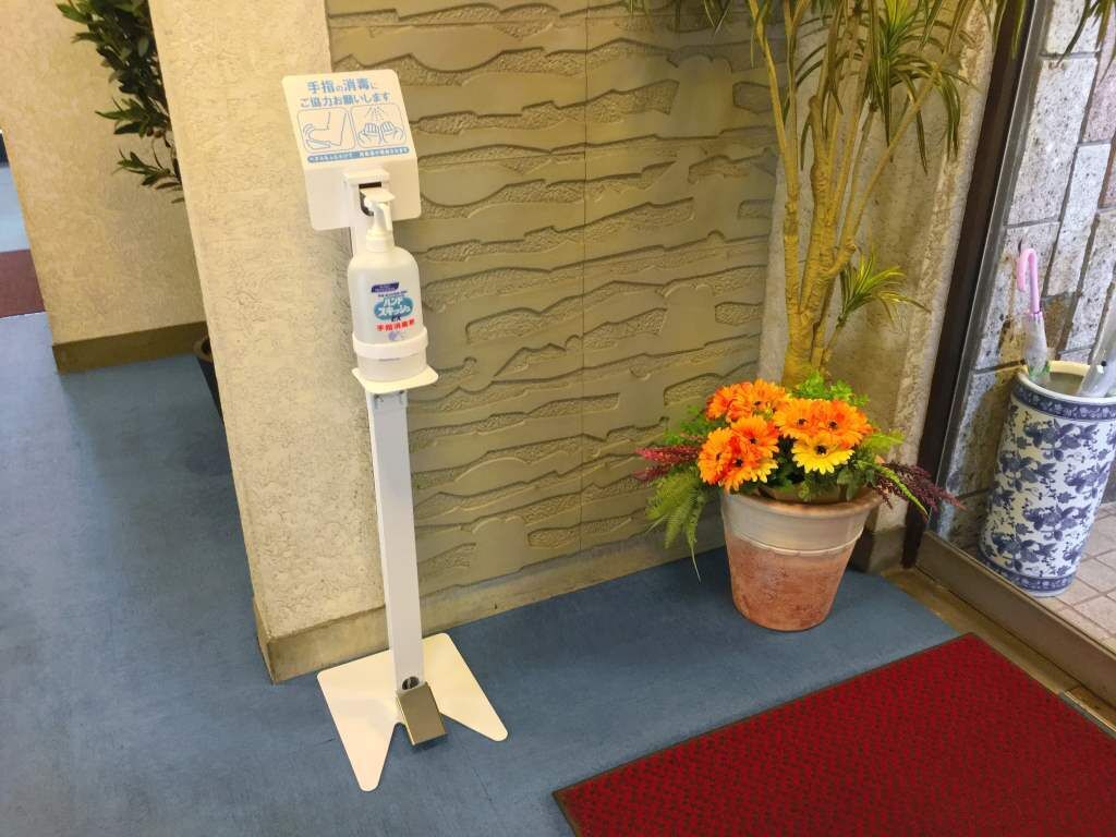 A hand sanitizer dispenser mounted on a wall, a potted plant with orange flowers, and a blue and red mat on the floor.