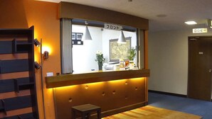 Un área de recepción con un mostrador de madera, un taburete pequeño, una alfombra azul y un cartel que indica la recepción.