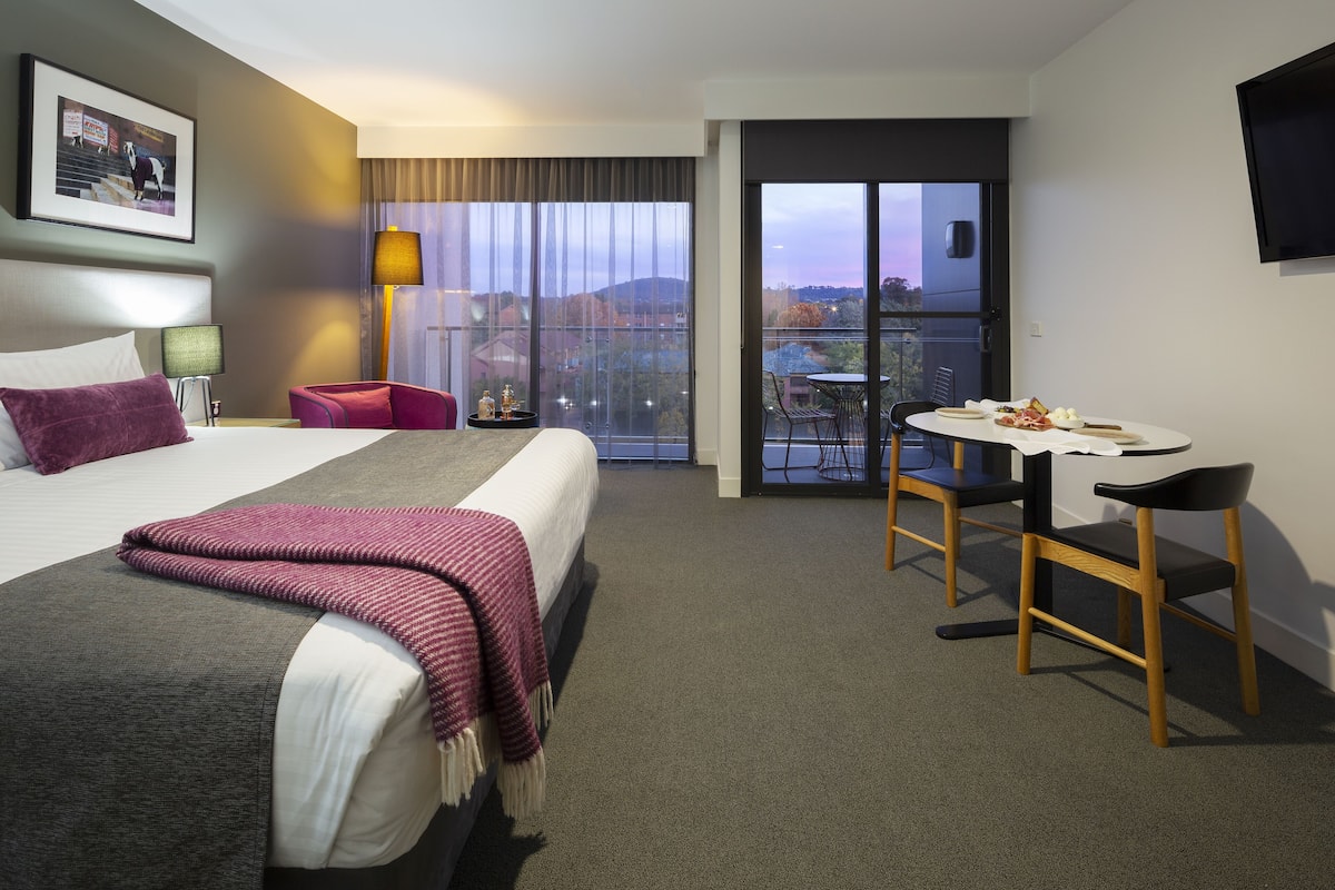 Ett hotellrum med en säng, ett skrivbord och en balkong med utsikt.
