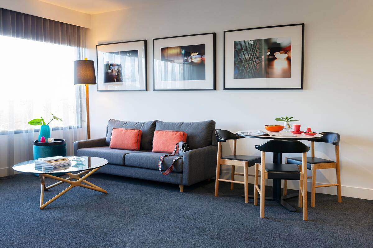 Ett modernt vardagsrum med en grå soffa, orange kuddar, ett runt soffbord och en matplats med ett litet bord och stolar.