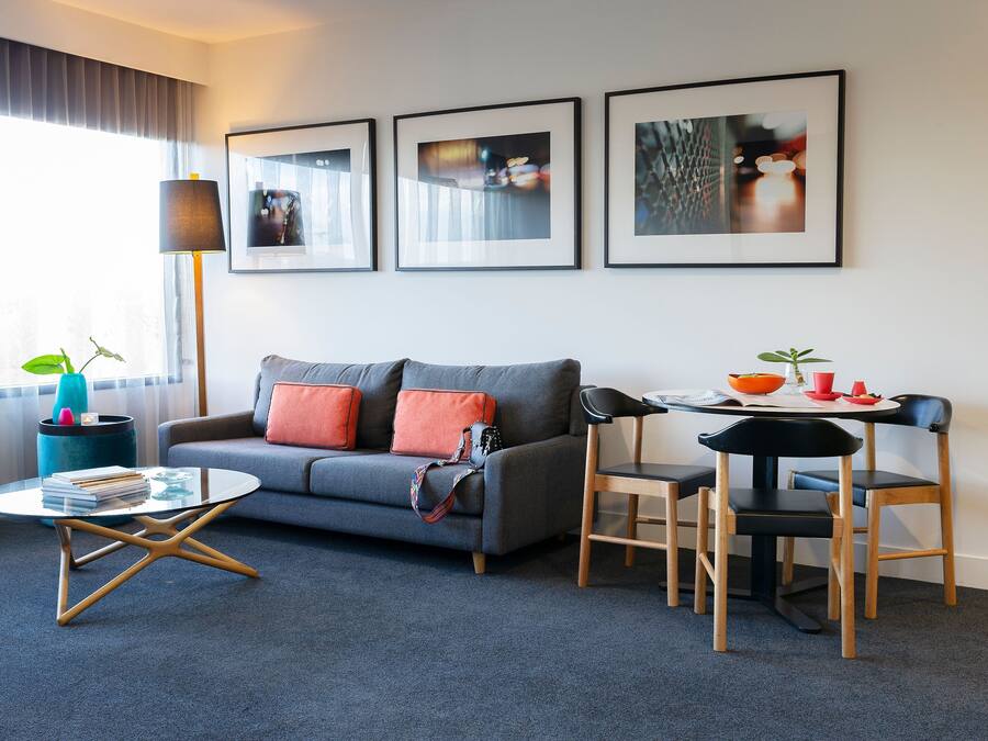 A modern living room with a grey sofa, orange cushions, a round coffee table, and a dining area with a small table and chairs.