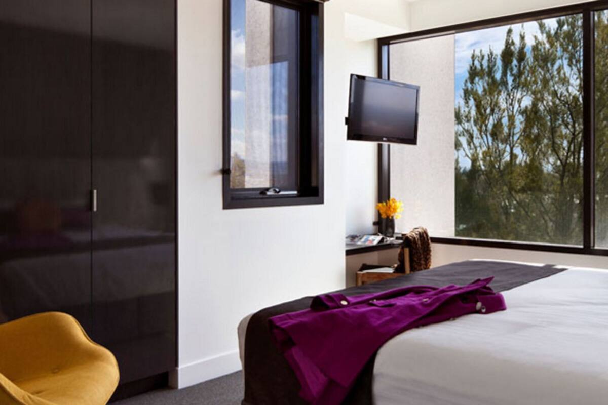 Ett modernt hotellrum med en stor säng, en tv och utsikt över träd genom fönstret.