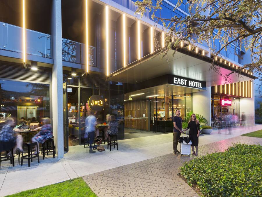 Un hotel moderno con fachada de vidrio, zona de estar al aire libre y un letrero que dice 'East Hotel'.