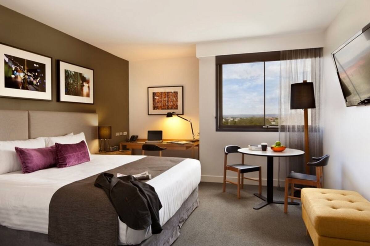 Ett hotellrum med en säng, ett skrivbord, en stol och ett litet bord med en skål.