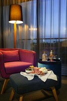 Una habitación moderna con un sofá rojo, un reposapiés azul y una pequeña mesa con comida y bebidas.