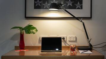 Un bureau avec un ordinateur portable, un vase rouge contenant une plante, un verre rempli de collations et une affiche encadrée accrochée au mur.