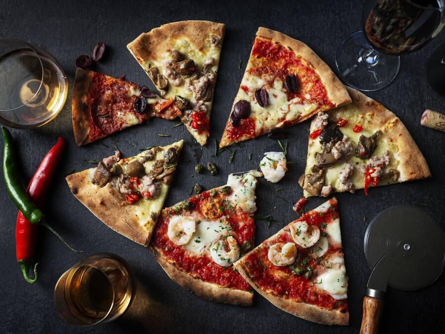 Pizza, jossa on erilaisia täytteitä, viinilasi ja korkinavaaja tummalla alustalla.
