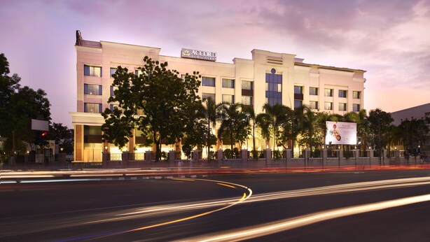 A multi-story hotel with a prominent sign, surrounded by trees and a well-lit street at dusk. - Accord Puducherry (Puducherry)