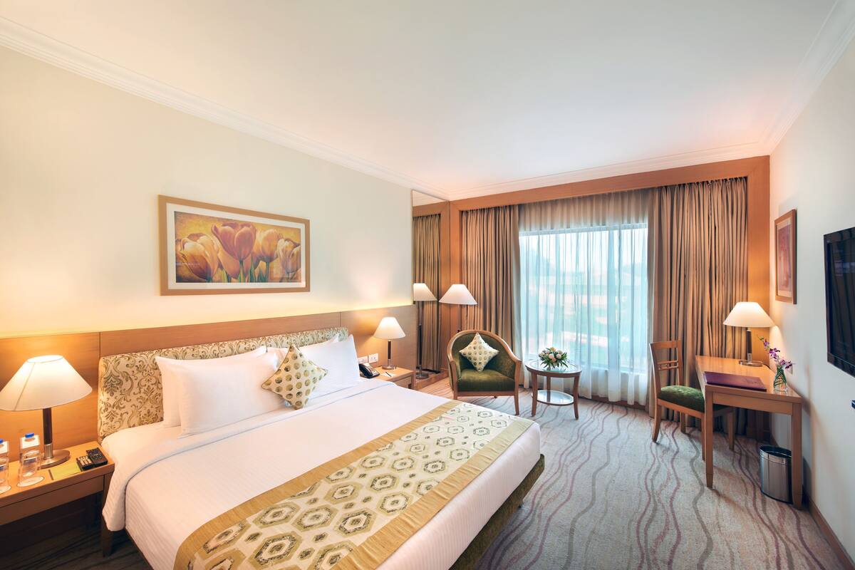 Habitación de hotel con una cama grande, dos sillas, un escritorio y una ventana con cortinas.