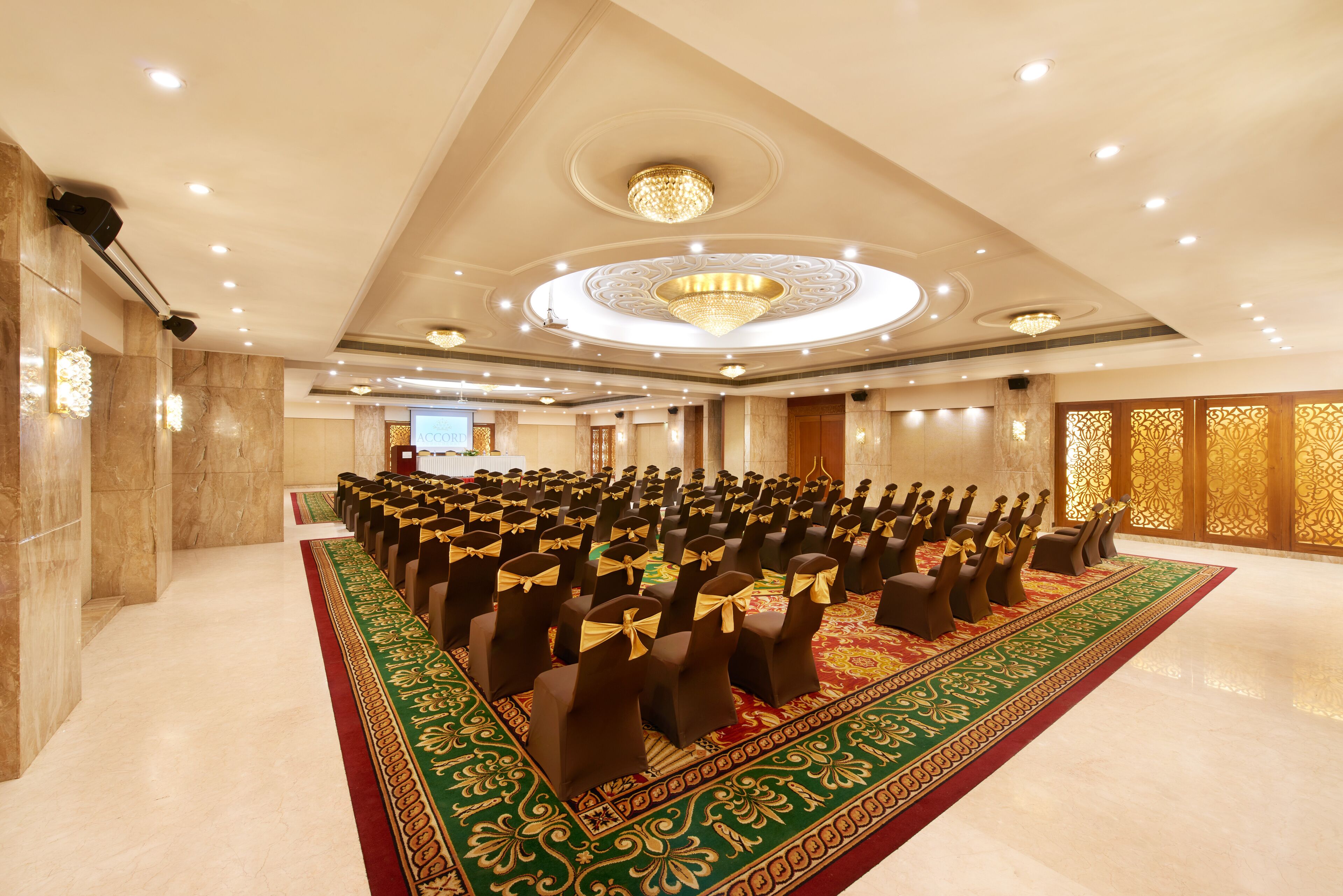 A large conference room with rows of chairs, a red carpet, and a chandelier.