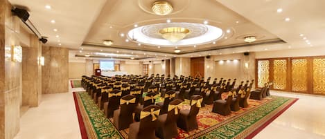Un amplio salón de conferencias con filas de sillas, una alfombra roja y un candelabro.