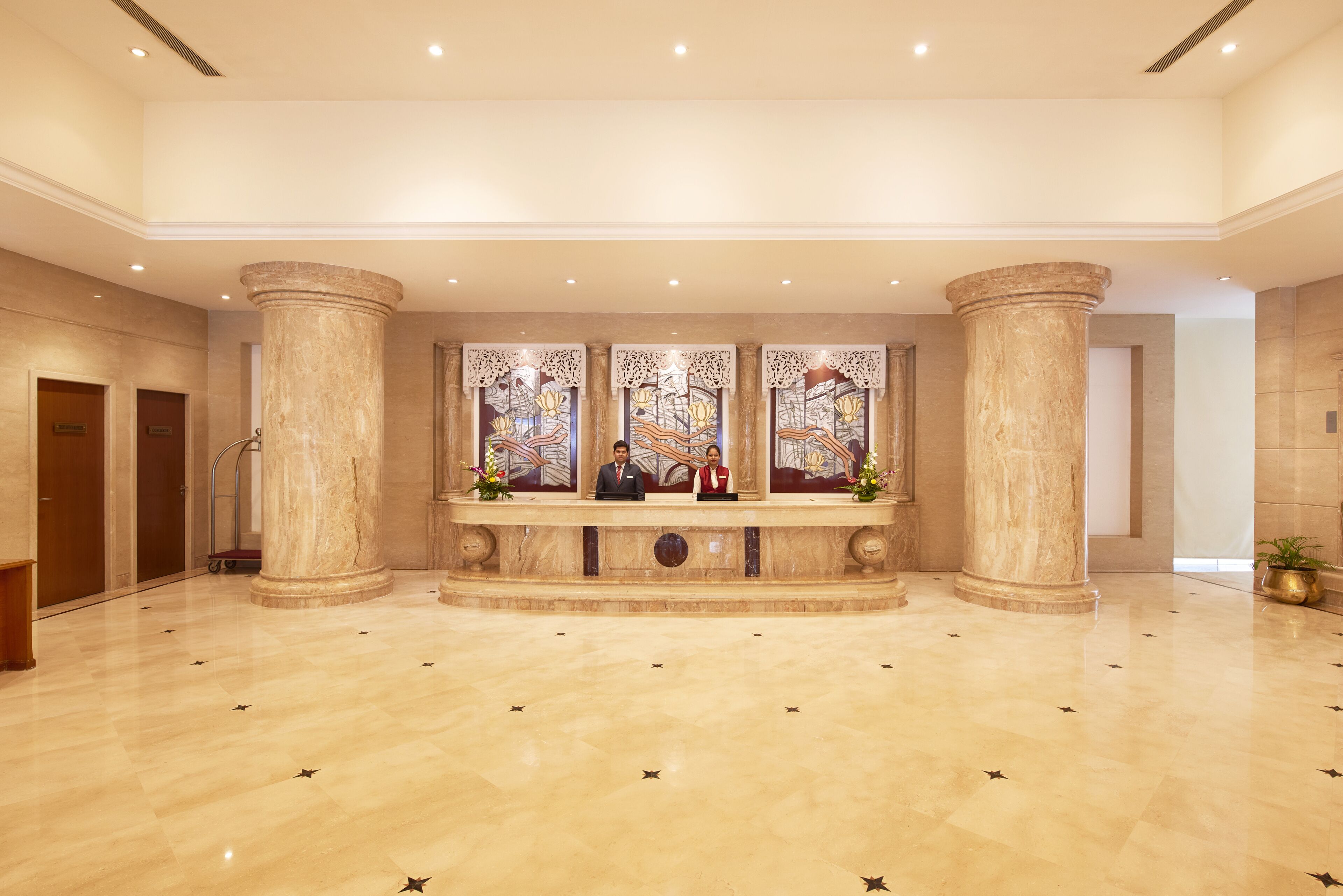 A spacious lobby with marble flooring, large columns, and a reception desk with two staff members.