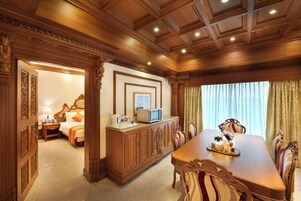 Habitación de hotel con techo de madera, una gran mesa de comedor y una cama con televisor sobre un mueble.