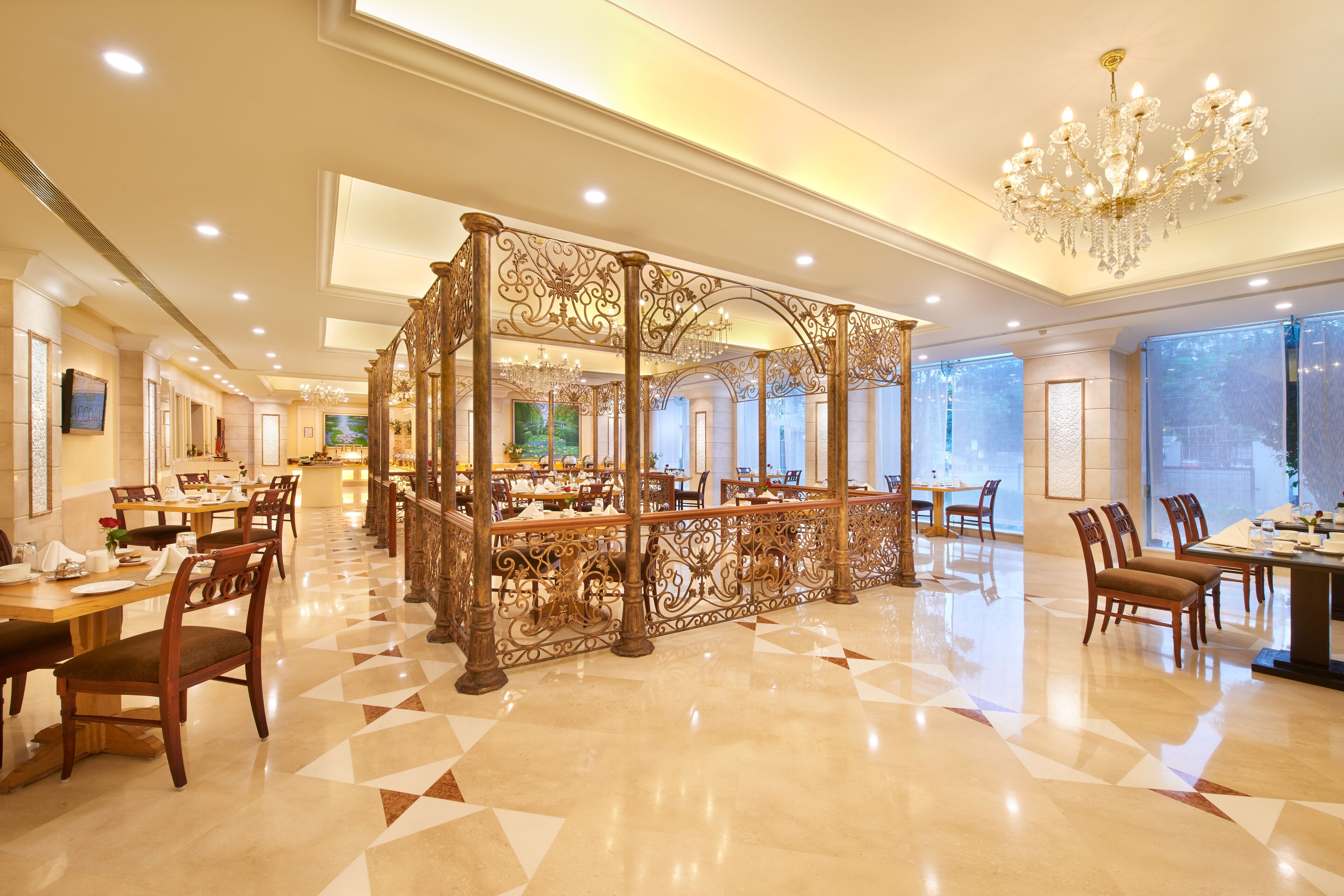 A spacious hotel dining area with ornate wooden partitions, chandeliers, and a polished floor.