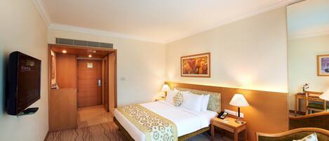 Una habitación de hotel con cama, mesita de noche, lámpara, sillón y televisor.