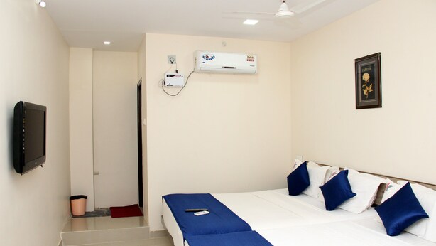 A hotel room with a bed, a TV, an air conditioning unit, and a ceiling fan. - KEK Accommodation (Chennai)