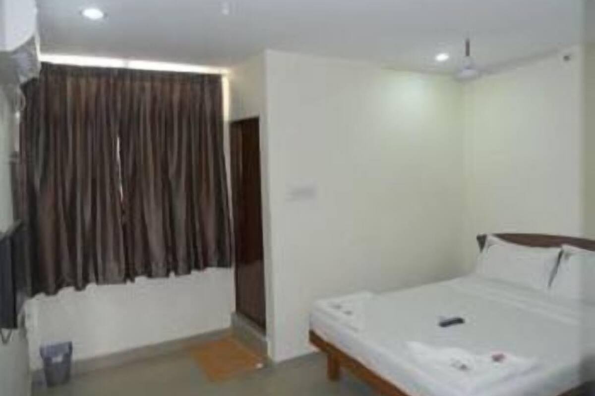 A hotel room with a single bed, a ceiling fan, a window with curtains, and a small bedside table.