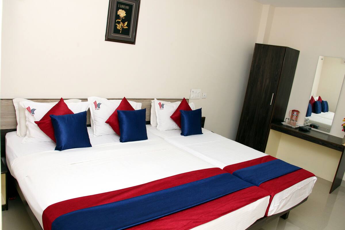 A double bed with white bedding, red and blue pillows, and a red and blue bedspread.