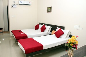 A hotel room with two single beds, each with red and white bedding, a vase of flowers on the nightstand, and a wall-mounted air conditioner.
