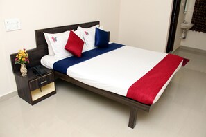 A neatly made bed with a white and red bedspread, a wooden headboard, and a nightstand with a vase of flowers and a phone.