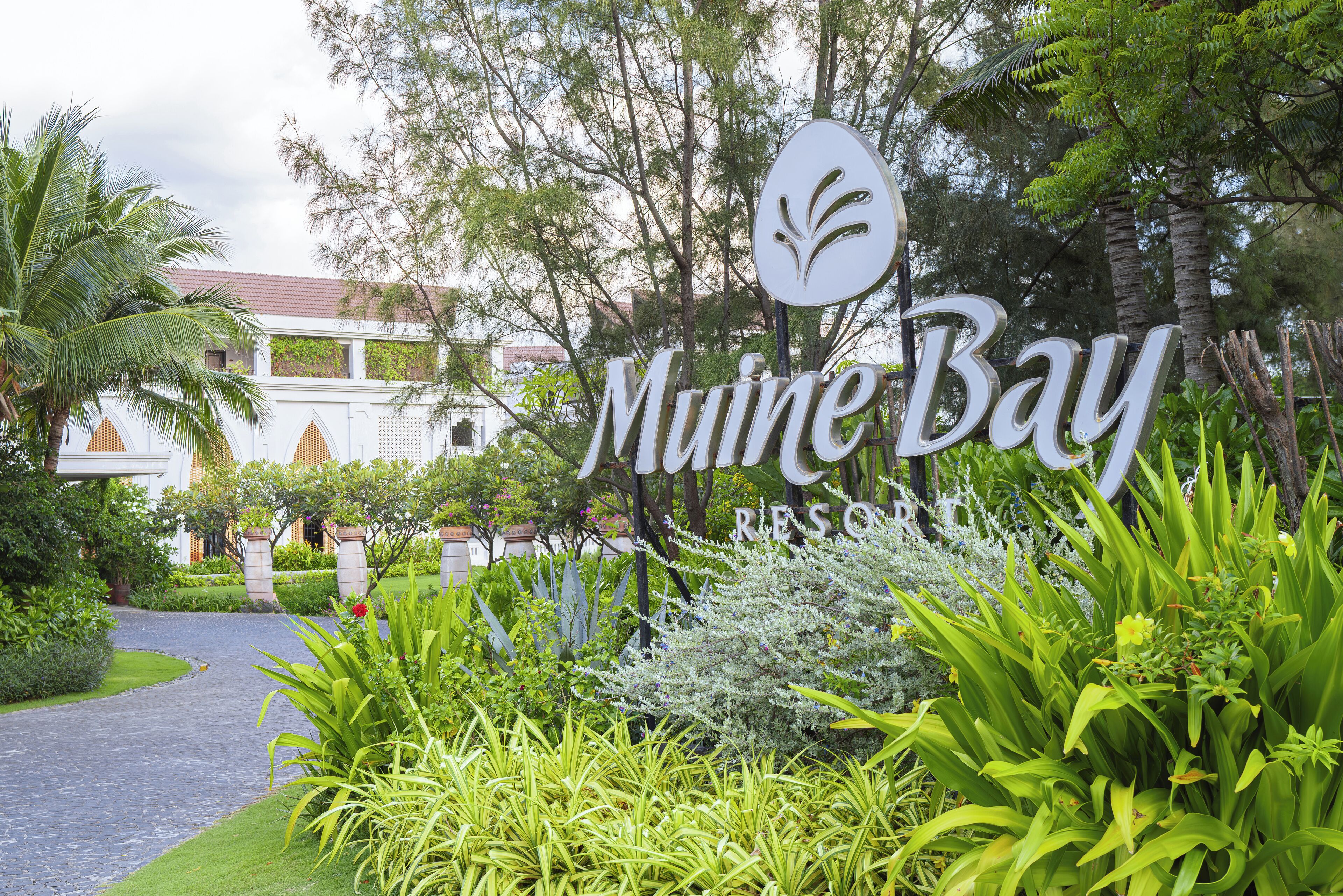 A sign for "Mune Bay Resort" surrounded by lush greenery and a pathway.